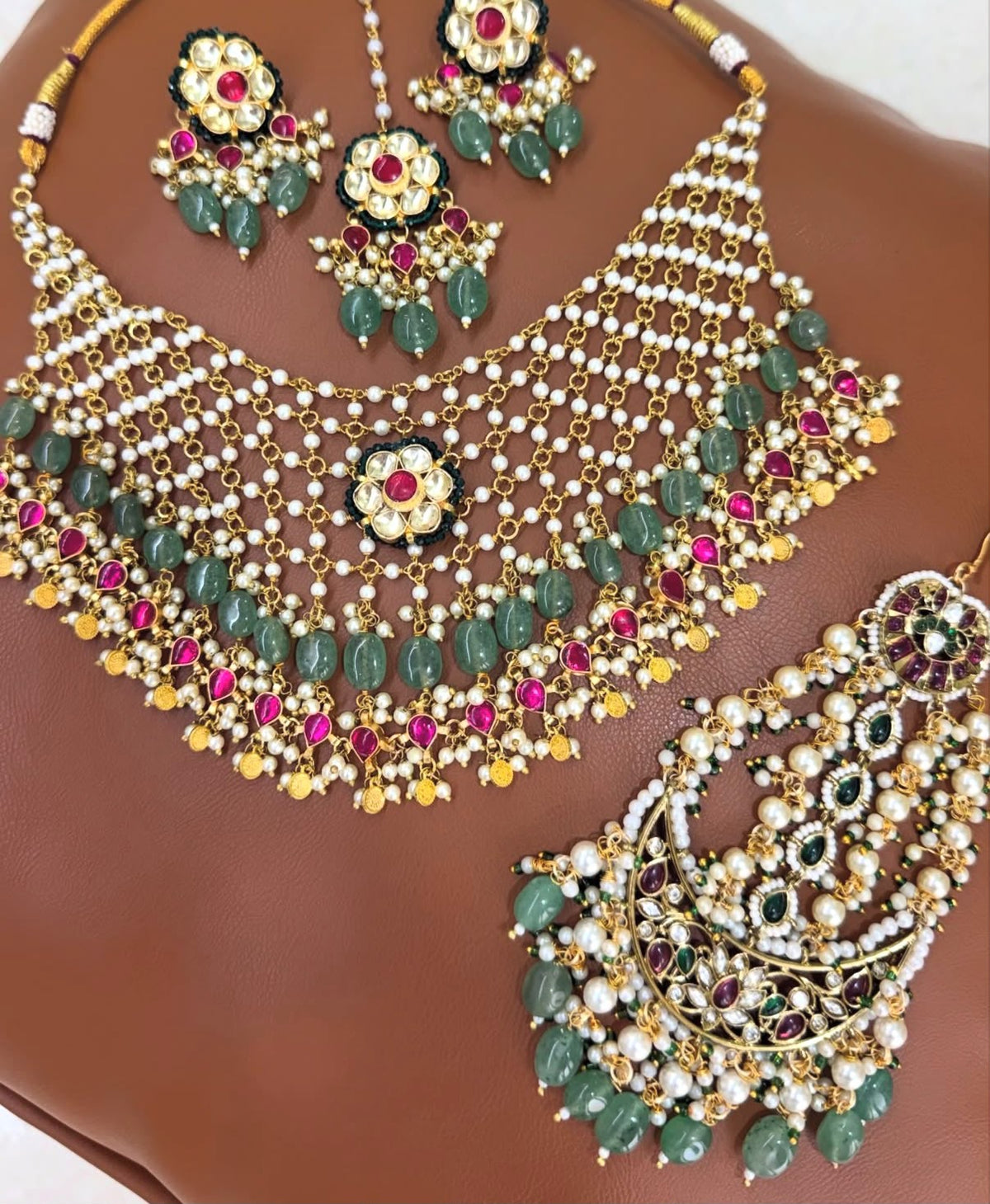 Nizami Emerald-Ruby Bridal Set flat lay - pearl choker with emerald green beads and ruby pink stones, passa, earrings and maang tikka in gold-tone brass